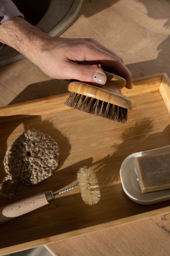 Close-up of hand holding a wooden brush on a bamboo tray with cleaning tools.