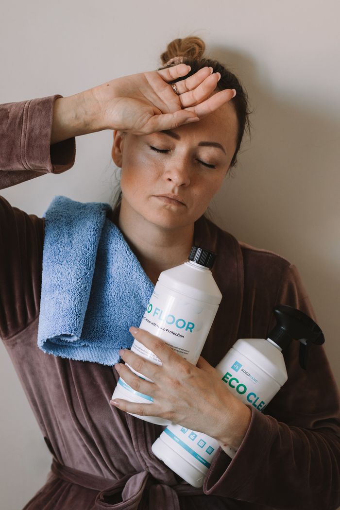 Woman holding eco-friendly cleaning products with blue microfiber cloth indoors.